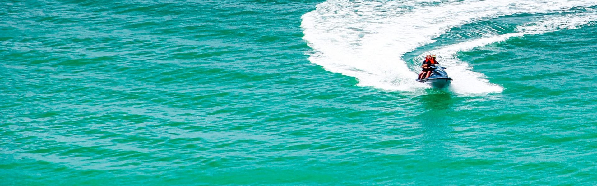 Moto de agua con dos personas trazando una curva sobre el mar turquesa de Alicante, vista aérea